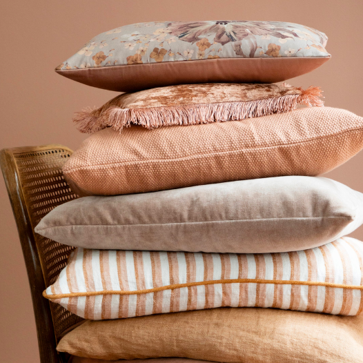 Stack of colorful pillows on a wooden chair against a plain background.